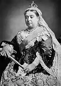 A black and white photo of a seated Queen Victoria in royal garb, with fan and crown.