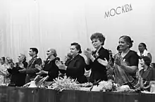 A line of clapping people standing behind a dias