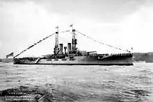 A large gray battleship sits in harbor